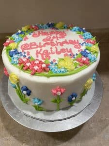 white cake with colorful flowers that says "happy birthday" on top