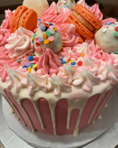 pink cake with macarons and sprinkles and cake pops on top